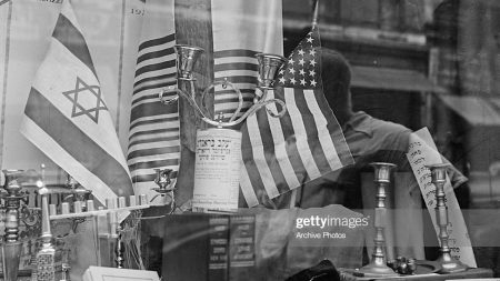 A shop window selling Jewish items on the Lower East Side of Manhattan, New York City, USA, circa 1955. A US flag is positioned opposite the flag of Israel, and a sign advertises Reverend I. Faber, 'Circumcision Surgeon'. (Photo by Archive Photos/Getty Images)